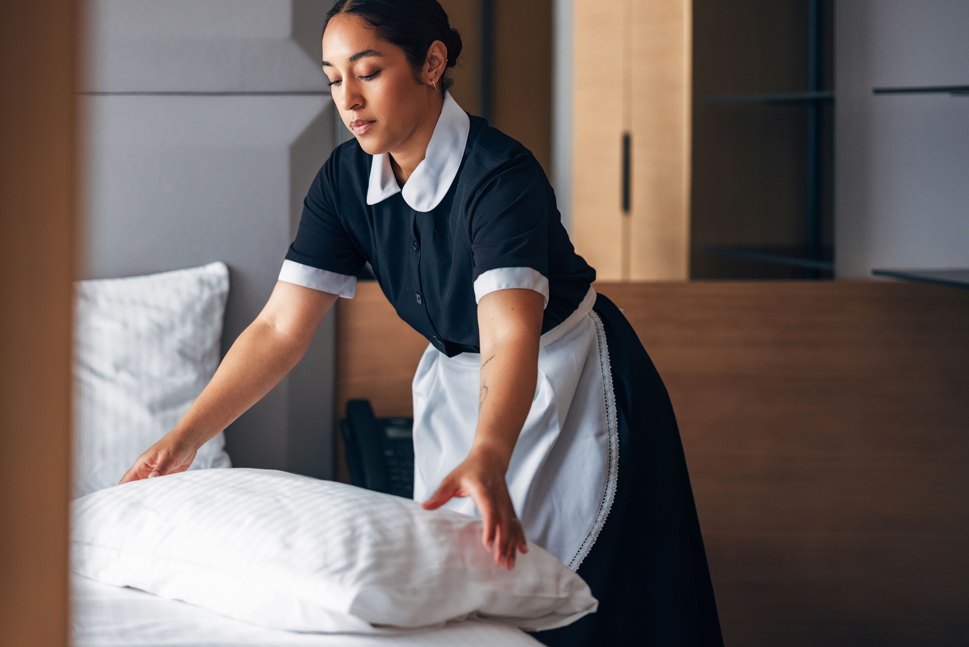 Hotel Staff Member Tidying White Bed With Professional Care